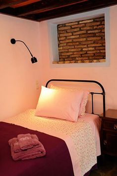 a bed with two pillows and blankets in a bedroom next to a lamp on the wall