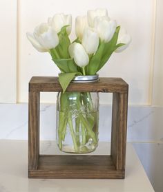 a mason jar filled with white tulips sitting on top of a counter