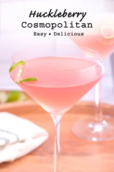 two pink cocktails sitting on top of a wooden table