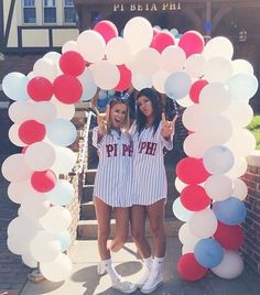 two girls in pinstripe outfits standing under a balloon arch