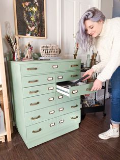 a woman standing in front of a green filing cabinet with drawers on top of it