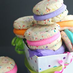 a box filled with lots of colorful cookies next to cupcakes on top of each other