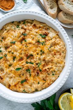 a casserole with cheese and herbs in a white dish next to lemon slices