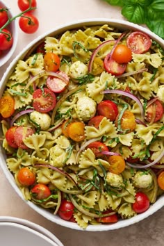 a bowl filled with pasta and vegetables on top of a white table next to tomatoes