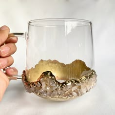 a person is holding a glass with some rocks in it and there is a piece of gold on the rim