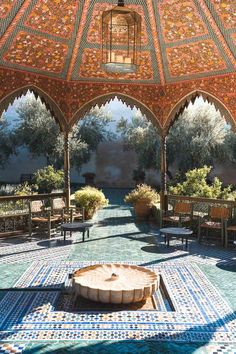 an outdoor seating area with tables and benches under a tiled roof, surrounded by potted trees