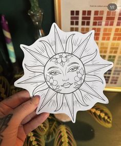 a person holding up a sticker with a sun design on it's face