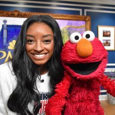 a woman with long black hair is holding a sesame character