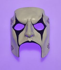 a white mask with black and silver details on it's face, against a purple background