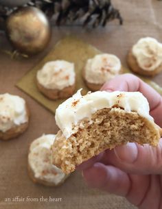 a person holding a half eaten cookie with frosting on it and pine cones in the background