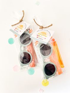 two packaged sunglasses sitting next to each other on top of a white table with confetti around them