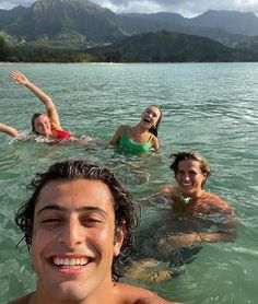 three people swimming in the water with mountains in the background