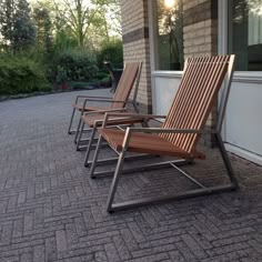 three wooden chairs sitting on the side of a building next to a brick sidewalk and trees