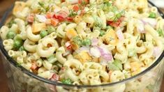 a glass bowl filled with macaroni salad on top of a wooden table