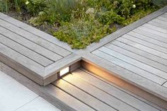 a wooden deck with plants growing on it and a light at the end that is lit up