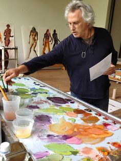 an older man is painting with watercolors on a large canvas in his art studio