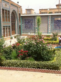 two people are standing in the middle of a garden with flowers and plants around it