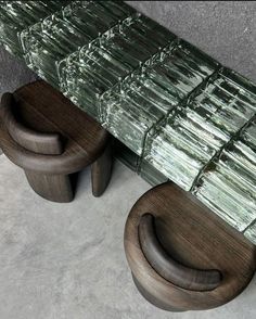 a glass table with two wooden stools next to it on concrete floored area