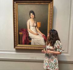 a woman standing in front of a painting with her hands on her hips and looking at it