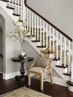 a chair sitting in front of a white stair case next to a table with a vase on it