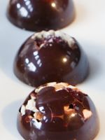 three chocolate covered donuts on a white surface