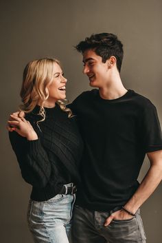 a man and woman standing next to each other in front of a gray wall smiling