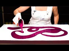 a woman in an apron is painting on a large piece of paper with purple paint