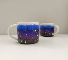 two coffee mugs with blue and purple designs on them, one has stars in the sky