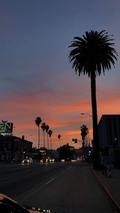 the sun is setting behind some palm trees on the side of the road with buildings in the background