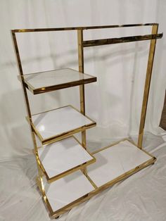 three tiered gold and white shelf with glass shelves on each side, in front of a white backdrop