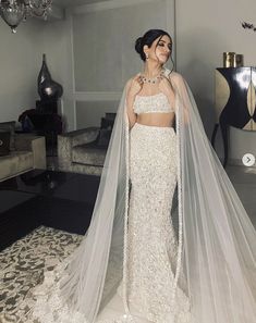 a woman in a white wedding dress with a veil on her head, standing next to a chandelier