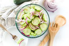 a glass bowl filled with cucumbers and onions next to wooden utensils