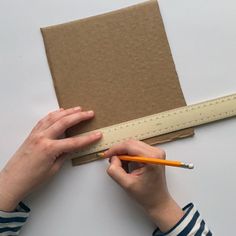 a person holding a pencil near a piece of cardboard with a measuring tape on it