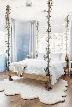 a bedroom with white bedding and hanging plants on the ceiling, along with wooden flooring