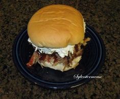 a large hamburger with meat and cheese on it sitting on a black plate in front of a granite counter top