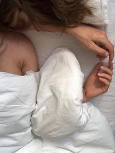 a woman laying in bed with white sheets