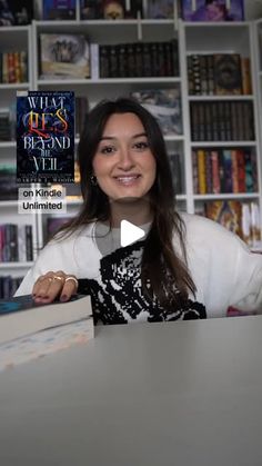 a woman sitting at a table in front of a book shelf with books on it