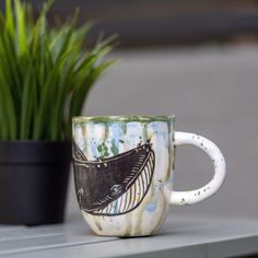 a coffee cup sitting on top of a table next to a potted green plant