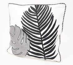 a black and white pillow with a palm leaf design on it, against a white background