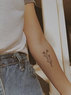 a woman's arm with a small flower tattoo on the left side of her arm