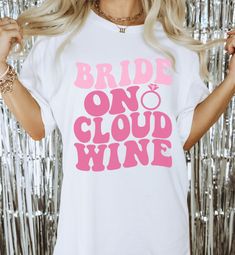 the bride on cloud wine t - shirt in white with pink print is shown next to silver tinsel