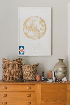 a wooden dresser topped with baskets next to a painting and vases on top of it