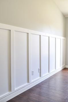 an empty room with white paneling and wood floors