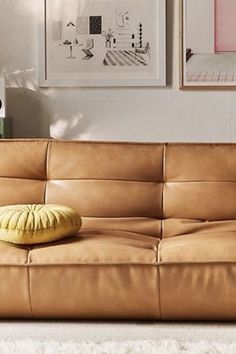 a tan leather couch with a yellow pillow on it in front of two framed pictures