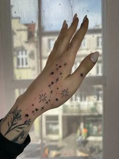 a woman's hand with stars and flowers on it, in front of a window