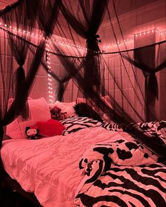 a bed with pink and black sheets in a room filled with lights, pillows and stuffed animals