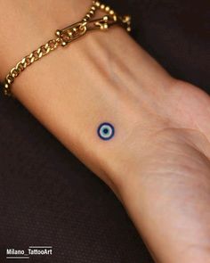 a woman's wrist with a blue evil eye tattoo on the left side of her arm