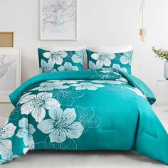 a bed with blue and white flowers on the comforter, next to two pictures