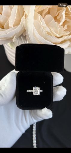 a diamond ring sitting on top of a black velvet box next to some flowers and pearls