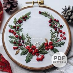 a christmas wreath with red berries and green leaves on white fabric surrounded by pine cones